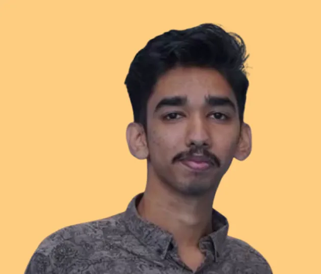 Jinso Raj, in a grey patterned shirt, cut out head and shoulders against a flat apricot background.