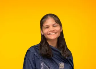 ഒരു ശോഭയുള്ള ഓറഞ്ച് സ്റ്റുഡിയോ പശ്ചാത്തലത്തിൽ നേവി കുർത്തയണിഞ്ഞ്, മുടി അഴിച്ചിട്ട്, ക്യാമറയിലേക്ക് നോക്കി പുഞ്ചിരിക്കുന്ന മേഘ ജിഭാകതെ.