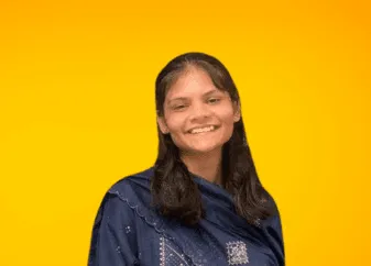मेघा जिभकाते नेवी कुर्ते में, खुले बालों के साथ, एक चमकीले नारंगी स्टूडियो बैकड्रॉप के सामने कैमरे की ओर मुस्कुराती हुई।