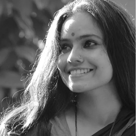 Black-and-white close-up of Anjali Thudippu smiling and looking away from the camera, her hair loose, a bindi on her forehead.