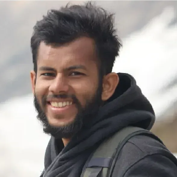 ഒരു തോളിൽ റാക്ക്സാക്കിന്റെ സ്ട്രാപ്പും ഇരുണ്ട ജാക്കറ്റും ധരിച്ച് നാജി മഹ്ഫൂദ് വെളിയിൽ നിന്ന് പുഞ്ചിരിക്കുന്നു, പശ്ചാത്തലം മങ്ങിയതും വ്യക്തതയില്ലാത്തതുമാണ്.